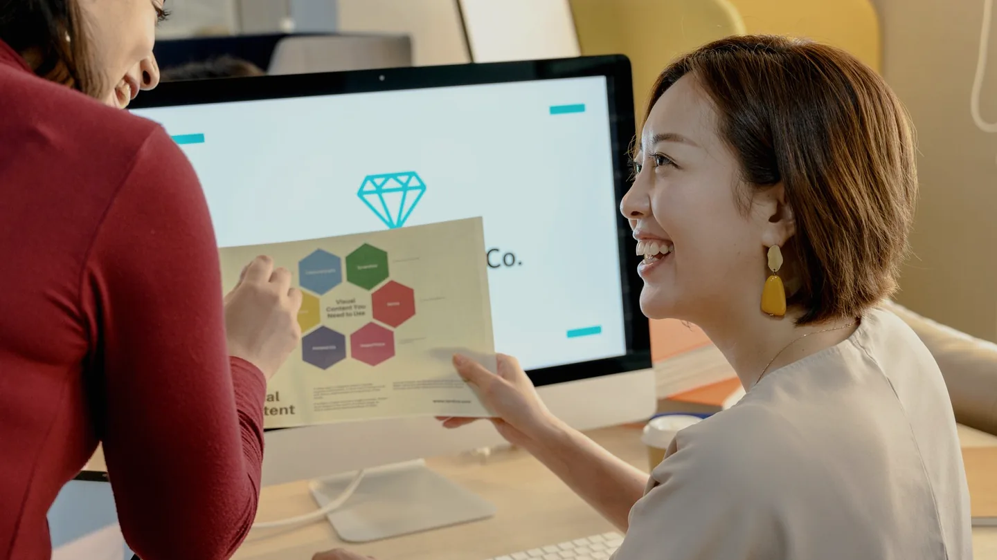 A colleague standing behind a seated worker, looking at their computer screen