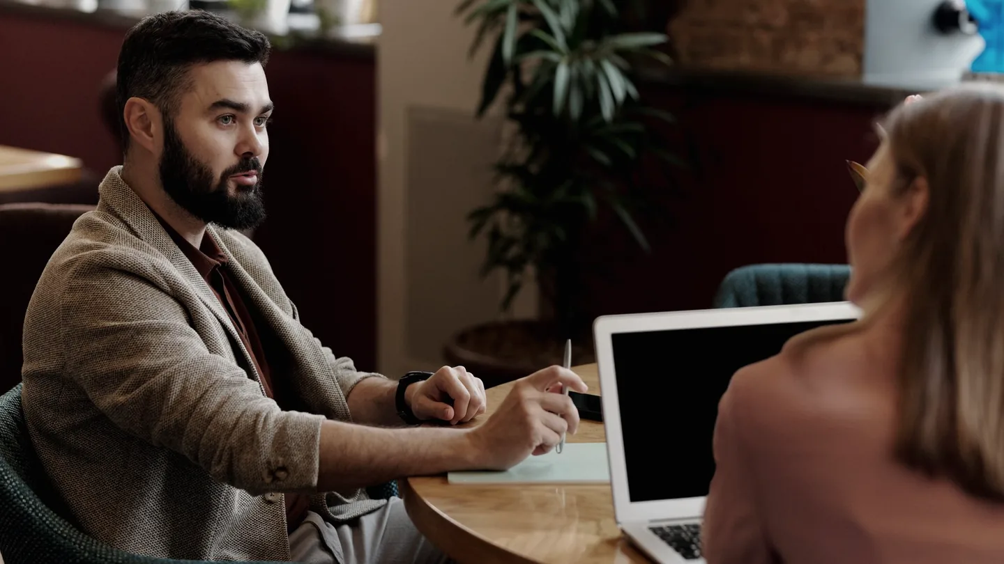 Dos personas conversando en una mesa pequeña dentro de un café con poca luz