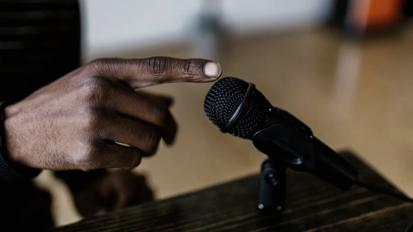 Una mano que se acerca para apagar una pequeña grabadora de voz sobre una mesa