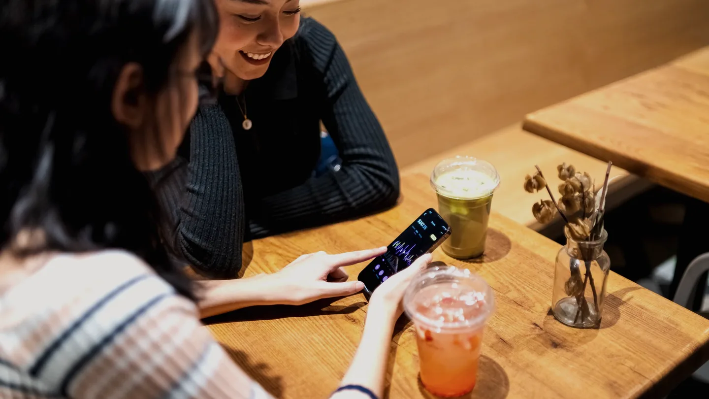 Dois amigos inclinados um para o outro olhando a mesma tela de celular à noite